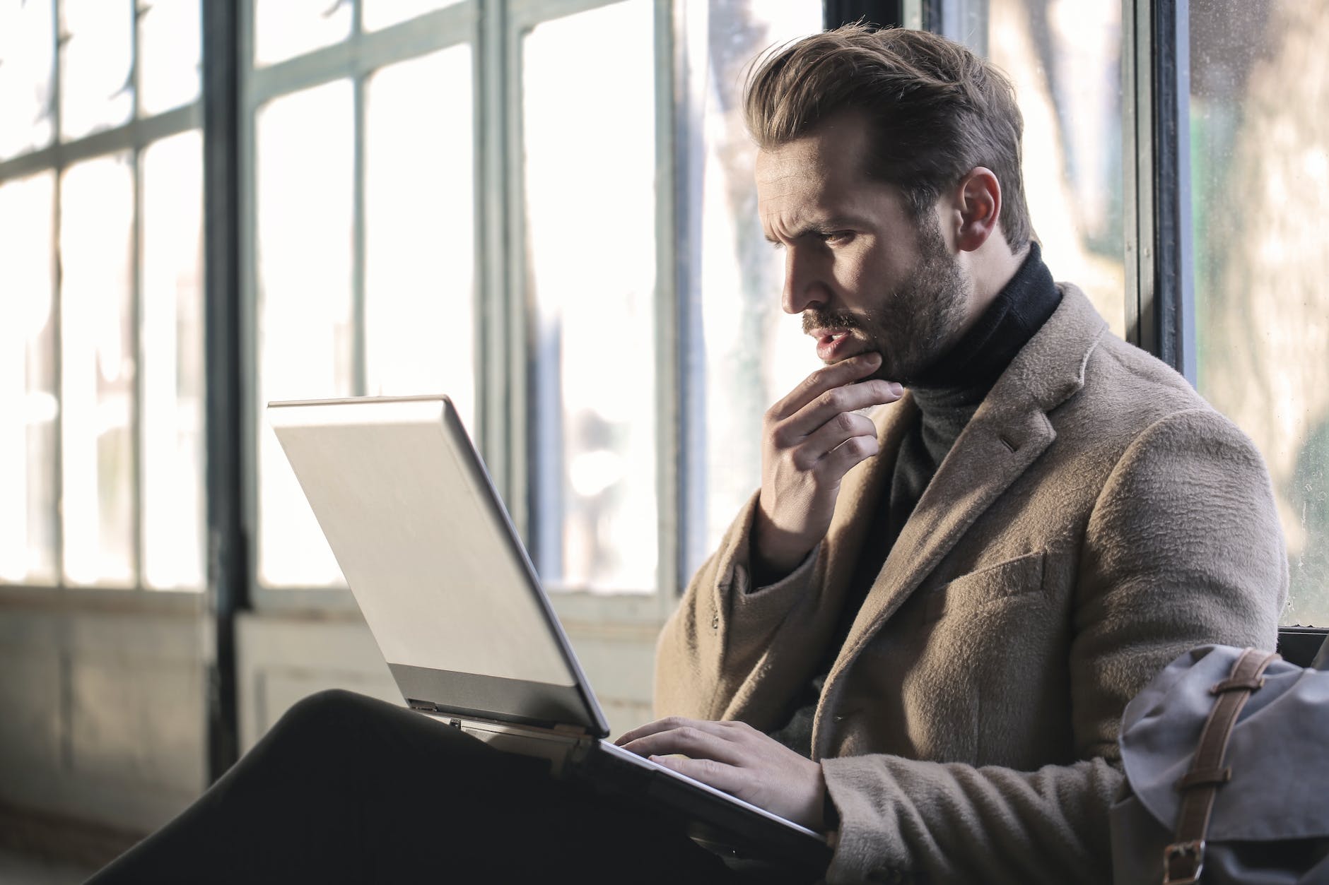 man wearing brown jacket and using grey laptop