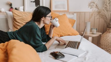 woman using laptop and drinking beverage in bed