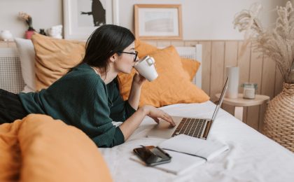 woman using laptop and drinking beverage in bed